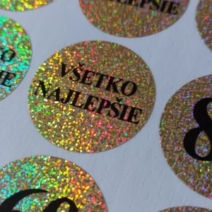 Detail zlatej trblietavej holografickej nálepky s čiernym textom