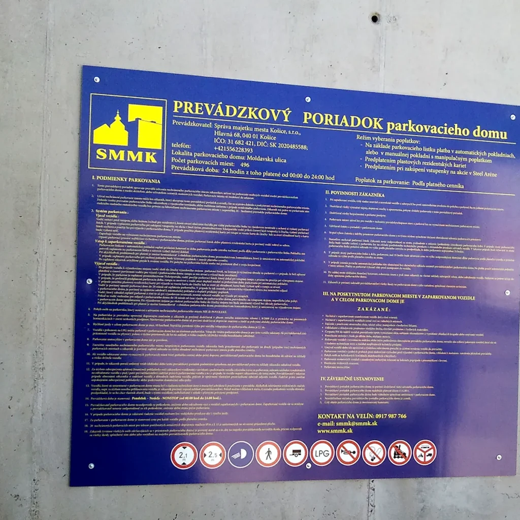 Veľká modrá tabuľa Prevádzkový poriadok parkovacieho domu s textom a piktogramami zákazov na betónovej stene