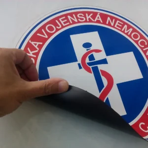 Ruka odlepuje okrúhlu magnetku z kapoty auta, vidno tmavohnedú magnetickú fóliu na rube