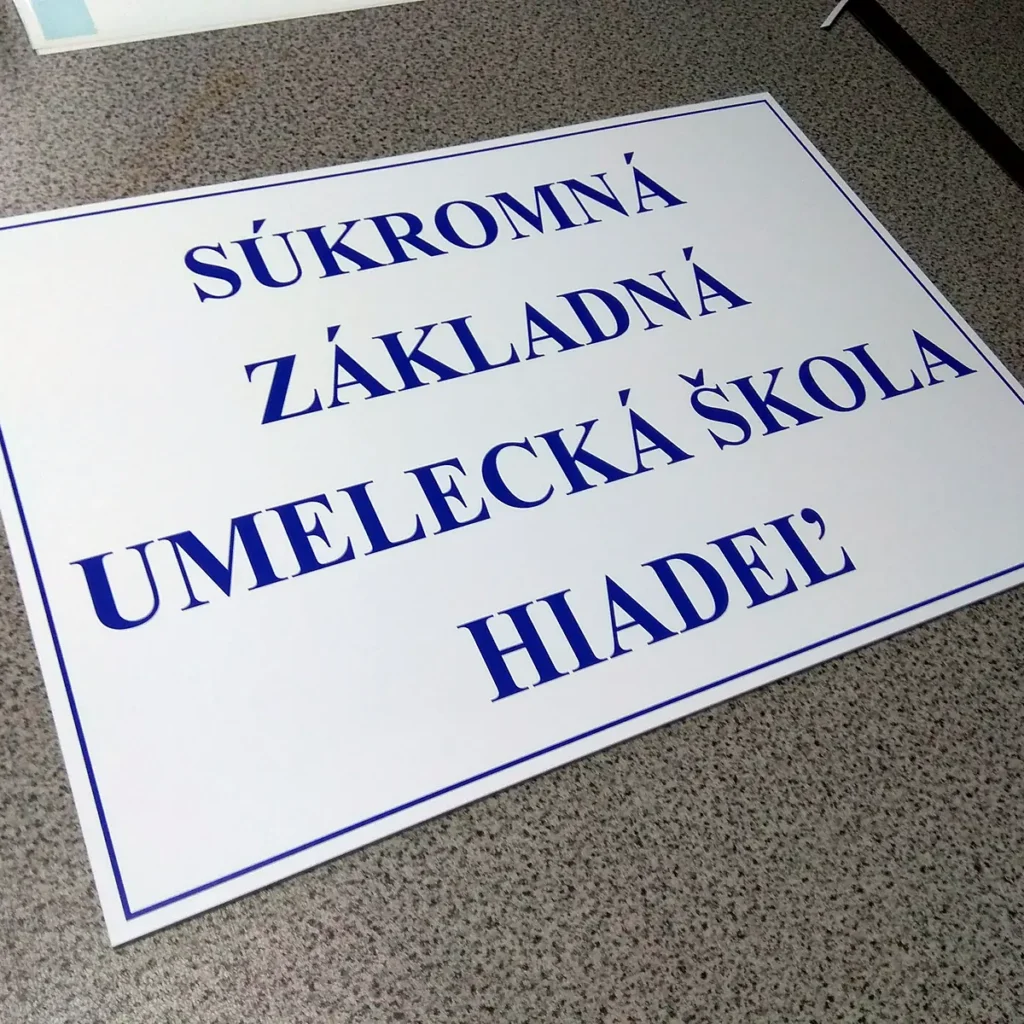 Biela tabuľa s modrým nápisom Súkromná základná umelecká škola a tenkým modrým rámikom na podložke